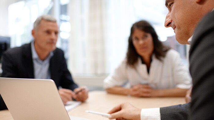 Three people at a business meeting listening to one give a presentation