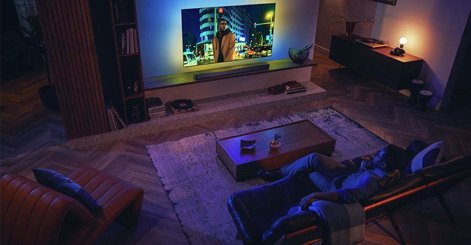 Soundbar'lı Philips Ambilight TV'nin keyfini çıkaran adam