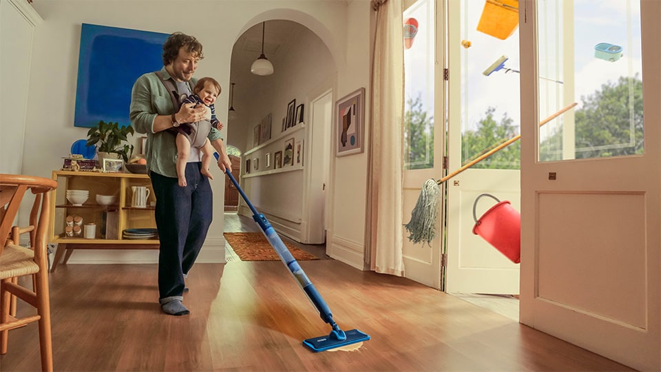 bebeğini taşıyan ve zemini temizlemek için Philips OneUp Elektrikli Paspas kullanan bir adam